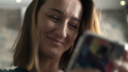 Pretty, Young Woman Texting on Smartphone Sitting in Cafe 30s