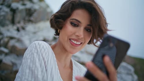 Woman Smiling at Phone on Rocky Beach