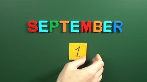 Hand sticking a sticker 1 September calendar day on school board. 1 date of September. First day