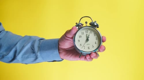 Business Man Shows the Time on the Alarm Clock 1205 O'clock Yellow Background
