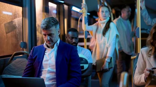 Vielbeschäftigter Geschäftsmann mittleren Alters, der an seinem Laptop arbeitet, während er nachts in einem überfüllten Bus nach Hause pendelt, s
