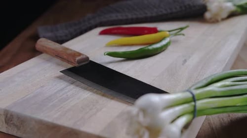 Camera dollies into wooden cutting board with green onions, knife and hot chili peppers.