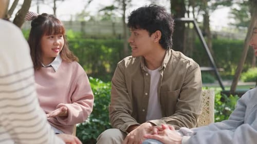 Small Asian group of people sit in a close circle and talk to a therapist in park.