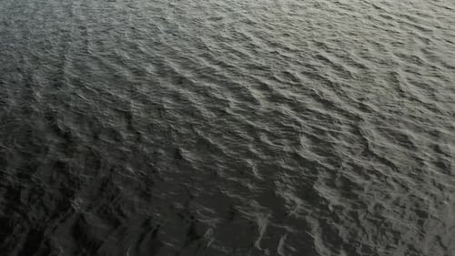 Aerial, very dark lake water with gentle waves rippling during the day