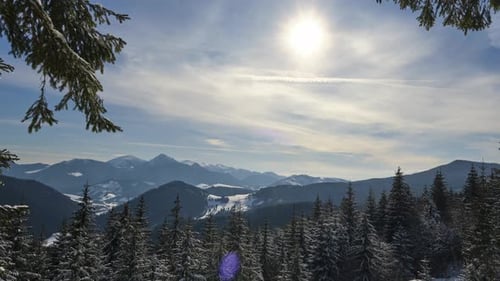 Berg- und hügelige Winterlandschaft Vom Wald aus bewegt sich die Sonne hinter den Wolken über den Himmel