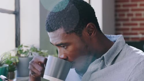 Young Man Uses Phone and Drinks Coffee Indoors