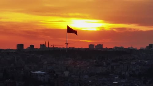 Cityscape at sunrise with waving flag in distance