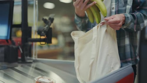La persona carga cuidadosamente los productos en una bolsa reutilizable, un comprador casual coloca los plátanos en su interior de forma respetuosa con el medio ambiente