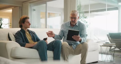 Two Men Discuss Tablet on Couch Indoors