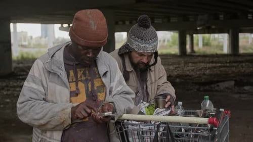 Two men under bridge look at items