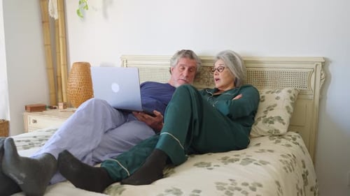 Senior Couple Relaxing on Bed with Laptop Indoors