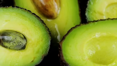 Drops of water fall on avocado fruits with leaves on a black background. Raw Fruits, healthy food.
