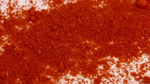 Red cayenne, paprika powder spice falling into white surface. Macro shot close up.
