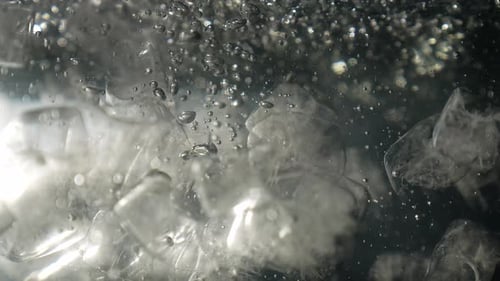 Ice Cubes Splashing into Water with Bubbles and Light