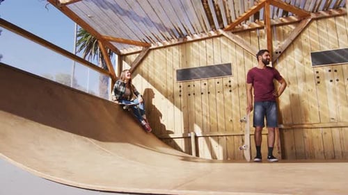 Video of happy diverse female and male skateboarders training in skate park