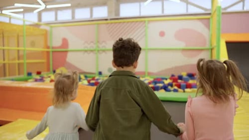 Deux petites filles et un garçon jouant sur une aire de jeux intérieure dans une fosse en caoutchouc mousse dans un trampoline en train de courir et