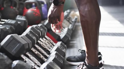 Selecting dumbbells, man preparing for workout in gym, focusing on fitness