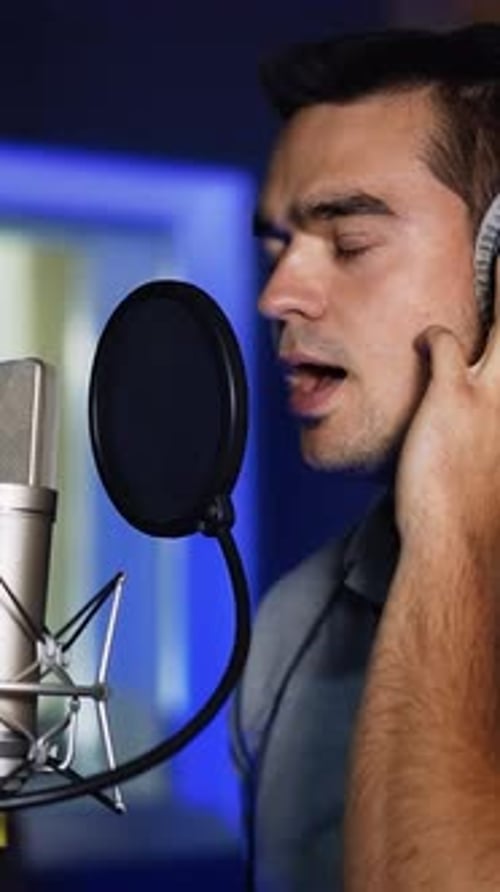 Caucasian singer wearing headphones holding them with his hands sings