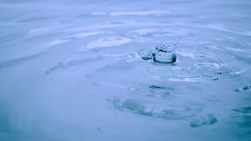 Drops of Water Falling on a Blue Liquid Surface and Forming Waves and Splashes