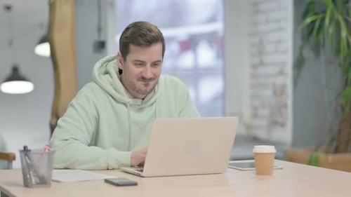 Young Man Celebrating Online Success on Laptop in Office