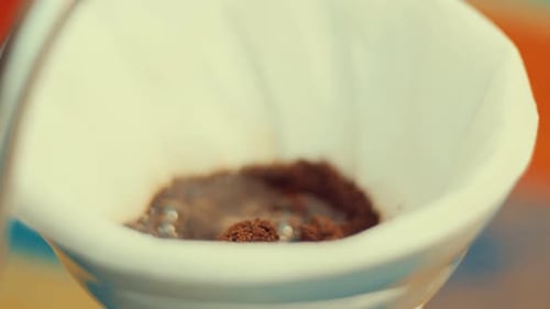weibliche Hand gießt heißes Wasser auf gemahlenen Kaffee in einer Pipette und macht Handkaffee mit Papierfilter