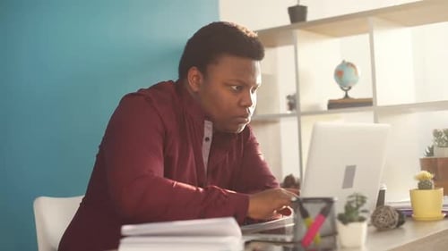 Concentrated Young African American Man Writing and Working on Laptop in Office Sunlight Business