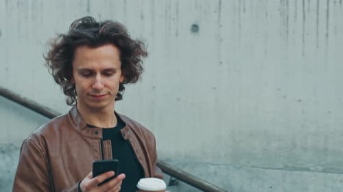 Man using smartphone and holding coffee outside