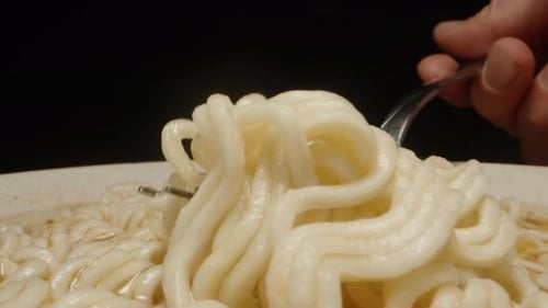I scoop up a piece of instant noodles with a fork. Dolly slider extreme close-up.