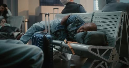 Exhausted Man with Luggage Sleeping on the Seats in Departure Lounge of Airline Hub