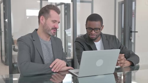 Two Adults Collaborate at Workplace Using Laptop