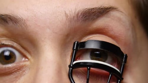 Woman uses eye lash curler on her lashes.