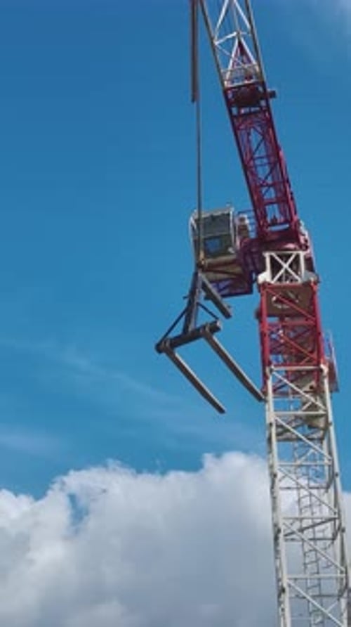 Vertical Video Aerial Perspective of a Tall Crane Lifting a Load High Against a Vibrant and Clear
