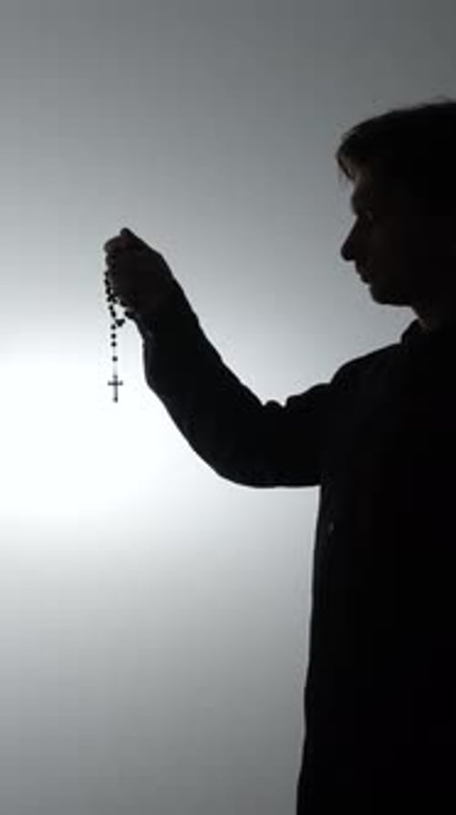 Teen Holding Rosary Silhouette Against Bright Background