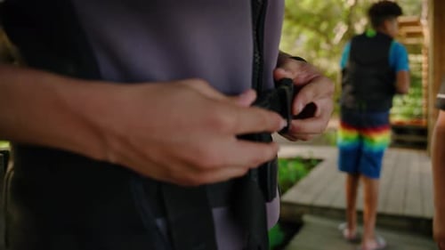 Male hands clasping buckle on life jacket flotation device while standing on dock near the water in