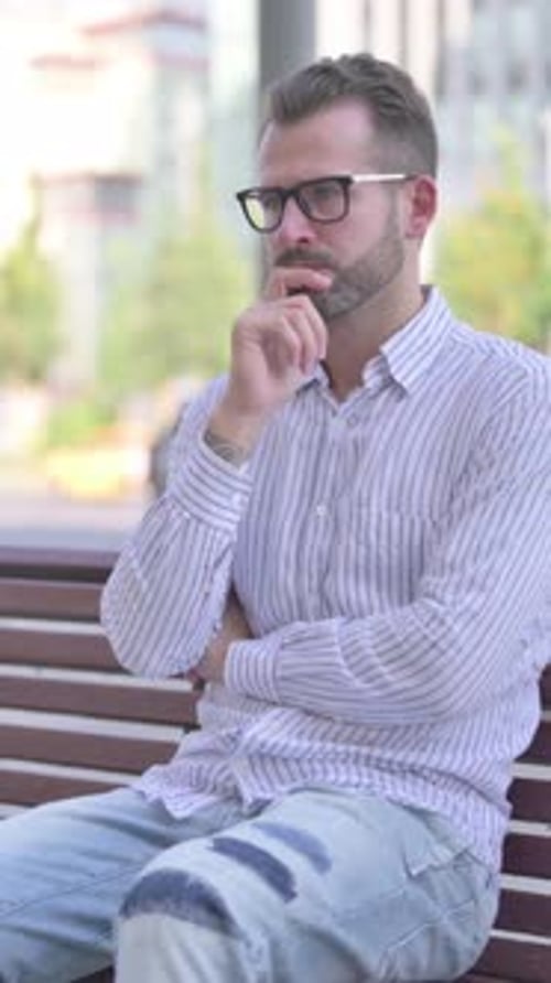 Pensive Young Adult Man Thinking while Sitting Outdoor on Bench, Vertical Video