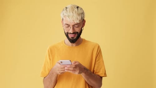 Smiling man with phone in his hands with mockup space isolated on yellow background in studio