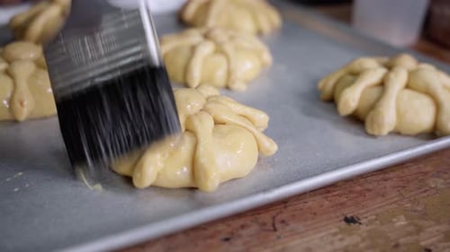 Glazing Mexican Bread of the Dead on Baking Sheet