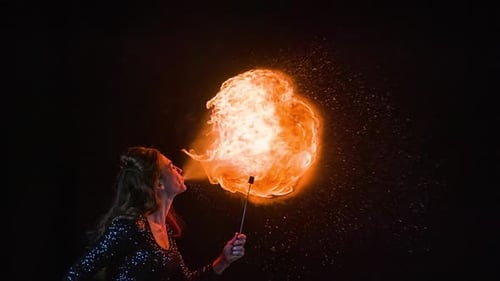 Woman Fire Breathing Against Black Background at Night