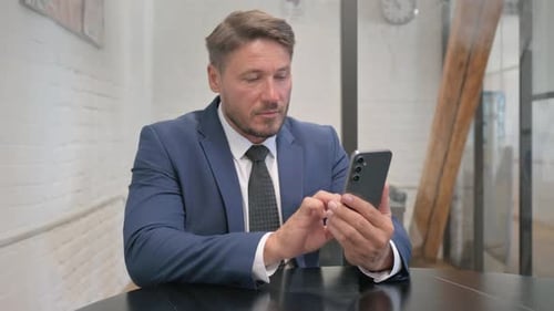 Man in Suit Using Smartphone at Office Table