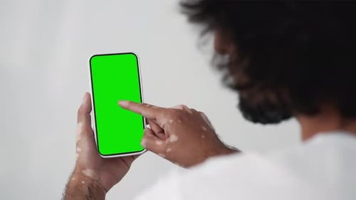 Young man using touch screen smartphone with green chroma key close-up