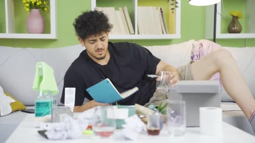 Young Adult Lies on Couch Reading in Messy Living Room