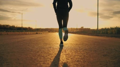 Young Slender Woman in Sportswear is Running in Sunset in Openair Rear View of Bottom Body Part