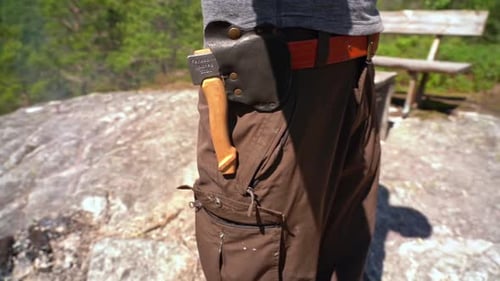 Handheld closeup of man at campsite with small axe in his belt - Sunny daytime slow motion clip with