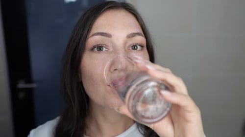 Darkhaired Woman Smiles Warmly with Sip of Fresh Water