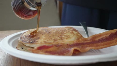 Pouring warm maple syrup on a short stack of pancakes for a traditional American breakfast - slow mo