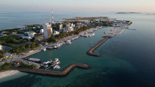 Aerial view of coastal town with a harbor, boats docked along the shore, and a protective breakwater