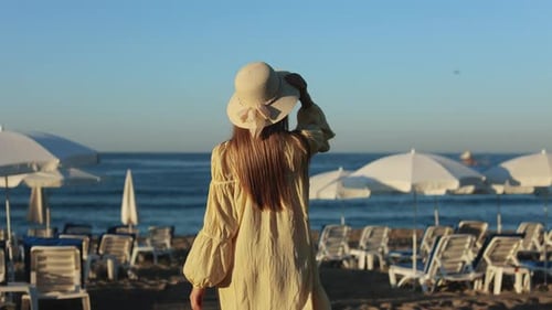 Woman in Straw Hat Enjoying Walk on Sandy Beach Near Sea