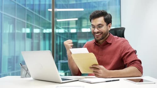 Joyful businessman reading letter with great news sitting at workplace in business office