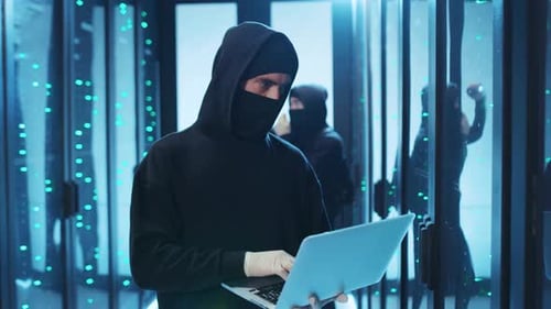 Figures in Hoodies with Laptop in Server Room