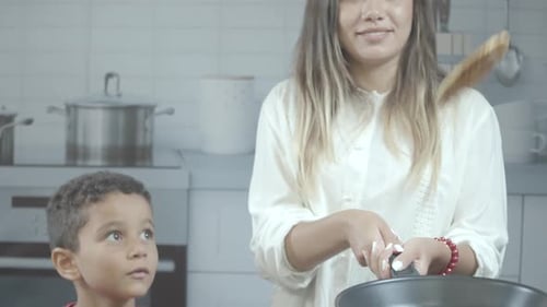 Beautiful young blonde girl with her kid, tossing pancake in the kitchen.